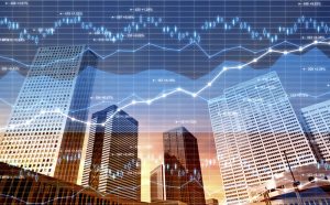 Panorama of a city business district with office buildings and skyscrapers and superimposed data, charts and diagrams related to stock market, currency exchange and global finance. Blue line graphs with numbers and exchange rates, candlestick charts and financial figures fill the image with a glowing light. Sunset light.